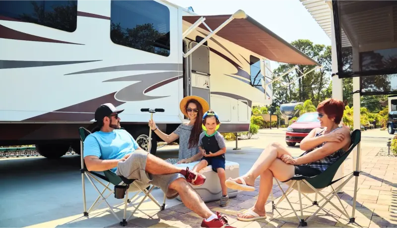 Une famille avec un jeune enfant se détend à l'extérieur de leur camping-car sous un auvent par une journée ensoleillée.