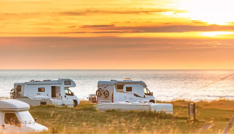 Plusieurs camping-cars sont garés près de la mer au coucher du soleil, créant une scène de voyage et de liberté.