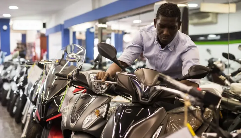 Un homme examine attentivement des scooters dans un magasin de motos, se penchant pour toucher un guidon.