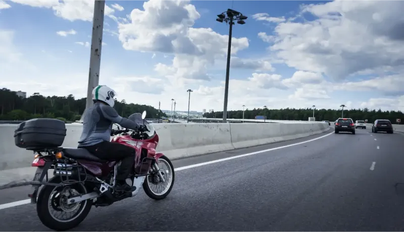Un motard roule sur une autoroute sous un ciel nuageux, avec une moto équipée de sacoches.