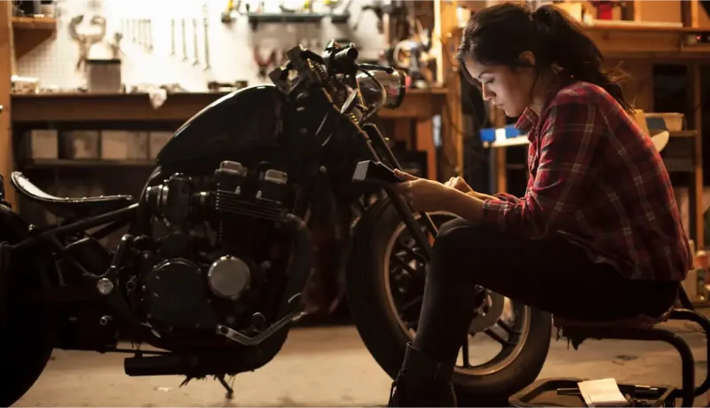 Une jeune femme mécanicienne concentrée travaille sur une moto dans un garage bien équipé.