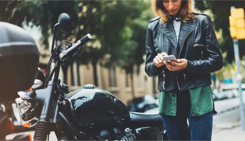 Une femme en blouson de cuir et jean vérifie son téléphone à côté d'une moto Harley-Davidson.