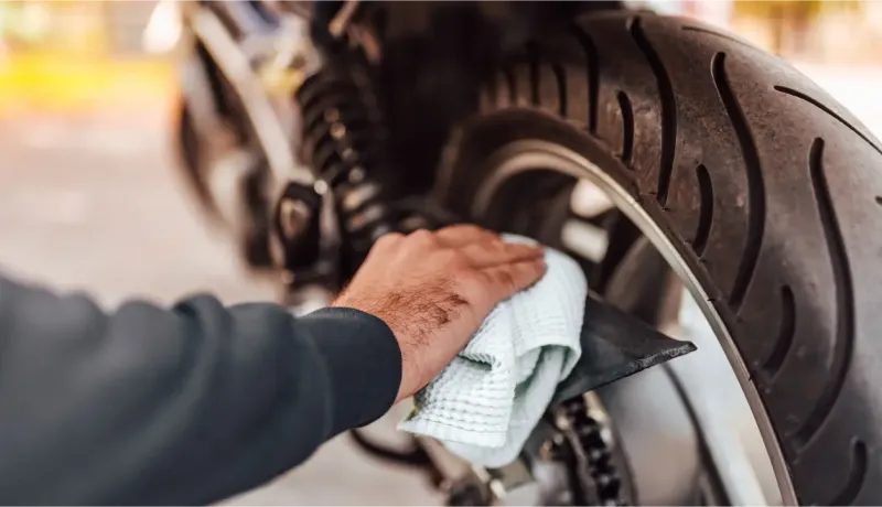 Une main nettoie le pneu arrière d'une moto avec un chiffon blanc et une jante noire.
