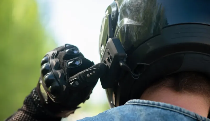 Gros plan sur une main gantée ajustant un intercom sur un casque de moto noir.