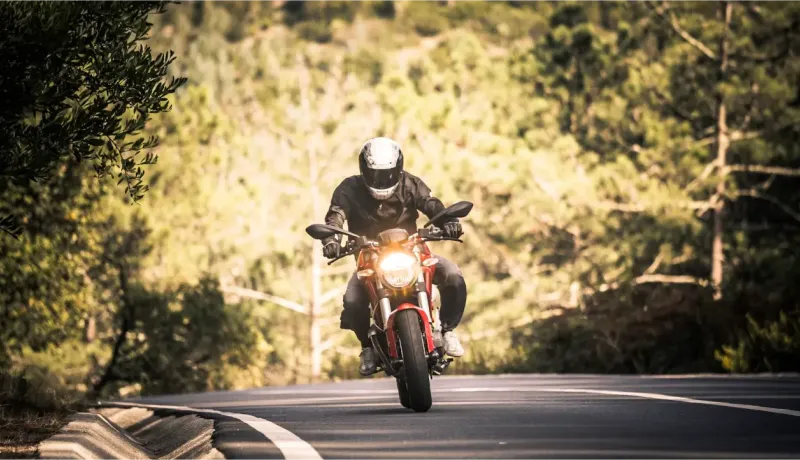 Un motard sur une moto rouge avec un casque blanc prend un virage sur une route de montagne.