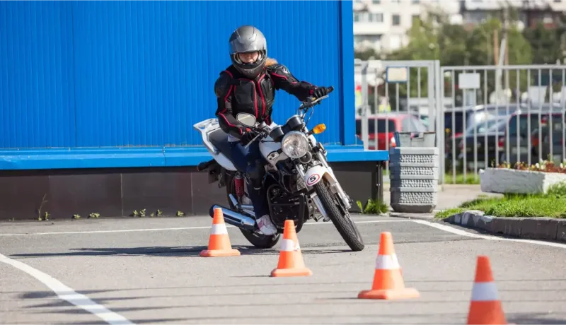 Une femme en casque et équipement de protection pratique la conduite de moto entre des cônes.