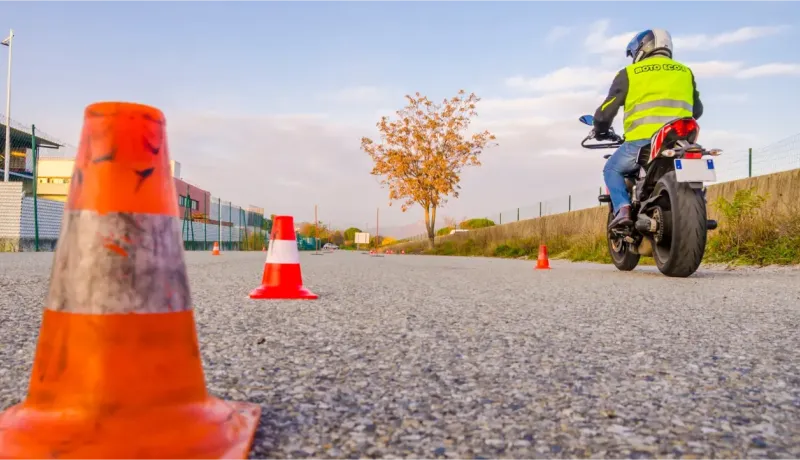 Un motard en gilet jaune fluorescent navigue entre des cônes de signalisation orange sur un terrain d'entra