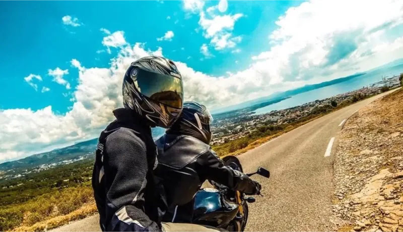 Deux motards en casque admirant la vue sur la mer depuis une route en lacets par temps ensoleillé.