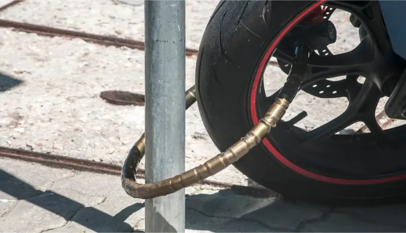Gros plan d'une chaîne antivol enroulée autour de la roue avant d'une moto et d'un poteau.