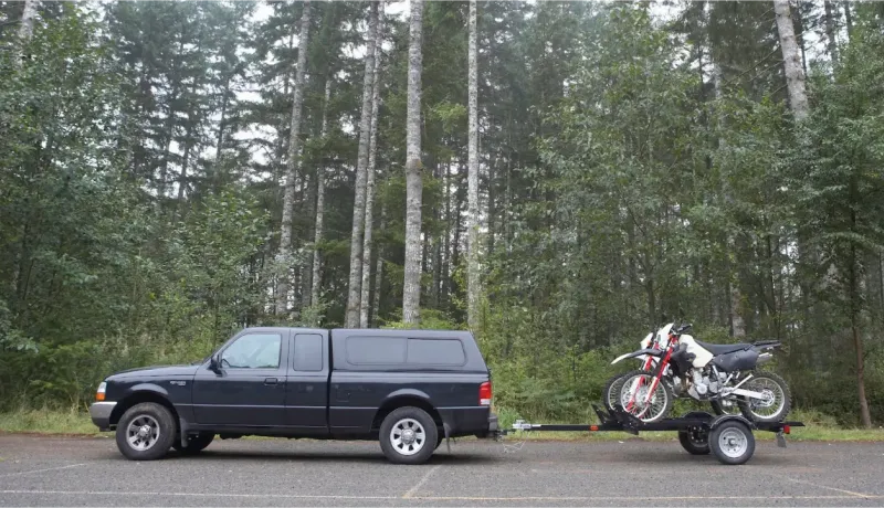 Un pick-up et une moto tout-terrain garés à l'orée d'une forêt dense de conifères.