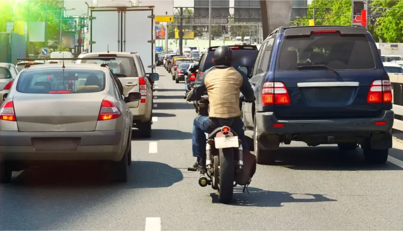 Un motard remonte une file de voitures dans les embouteillages.