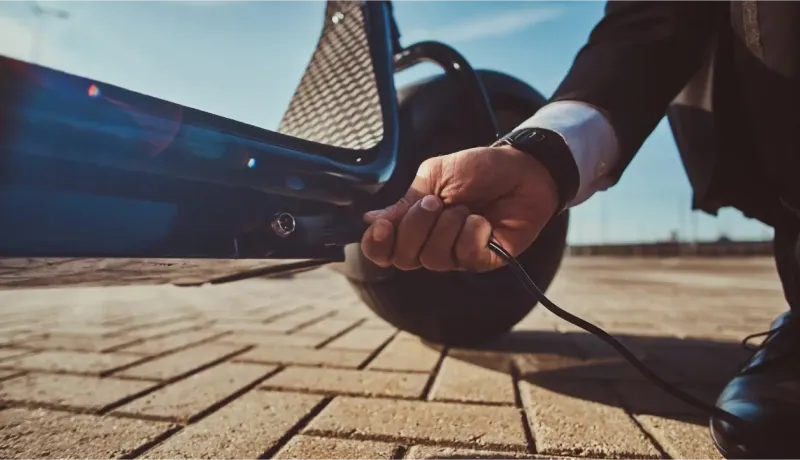 Gros plan sur une main branchant un câble de chargement à une trottinette électrique sur un sol pavé.