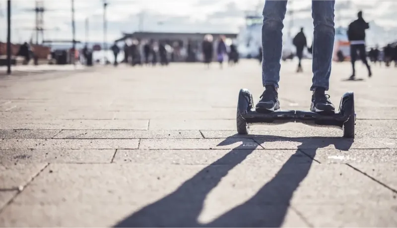 Gros plan sur les pieds d'une personne debout sur un hoverboard sur un trottoir pavé.
