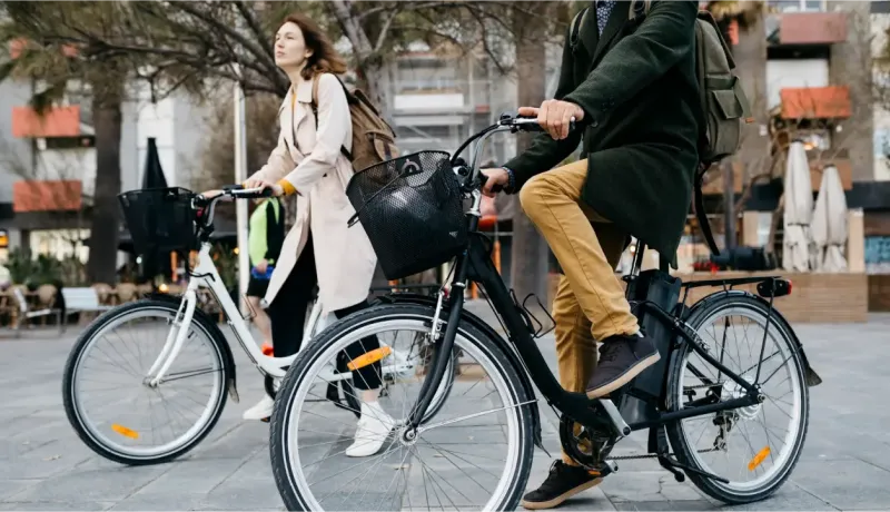 Un homme et une femme marchent à côté de leurs vélos de ville, avec des paniers à l'avant, en milieu urbain.