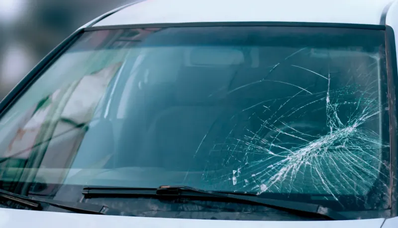Un gros plan sur un pare-brise de voiture fissuré, montrant un impact en forme d'étoile.