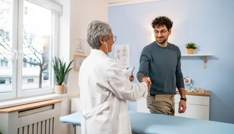Un médecin serre la main d'un patient souriant en cabinet.
