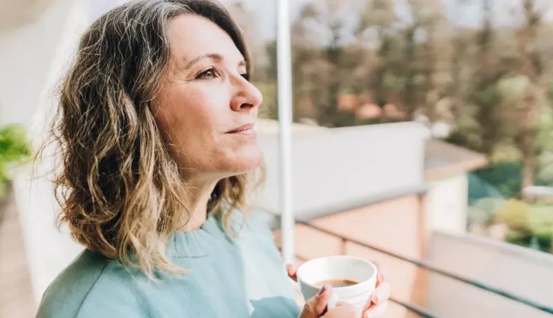 Une femme regarde au loin avec une tasse à la main, moment de réflexion.