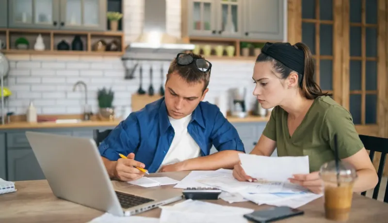 Jeune couple examinant des papiers et utilisant un ordinateur.
