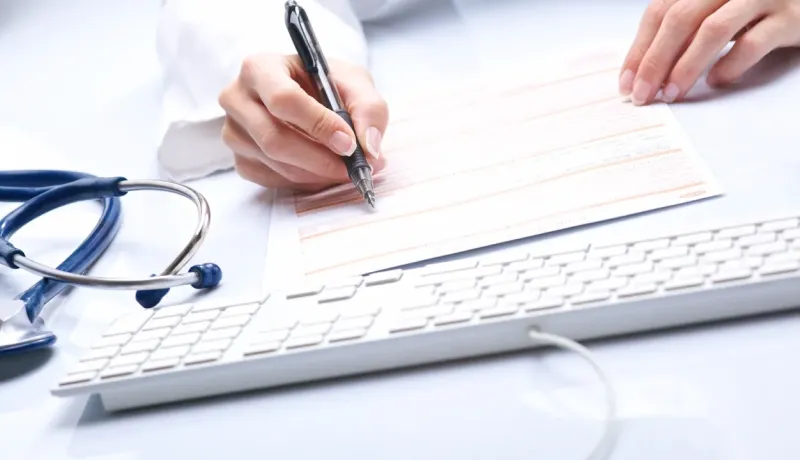 Médecin écrivant sur un formulaire, stéthoscope à côté.