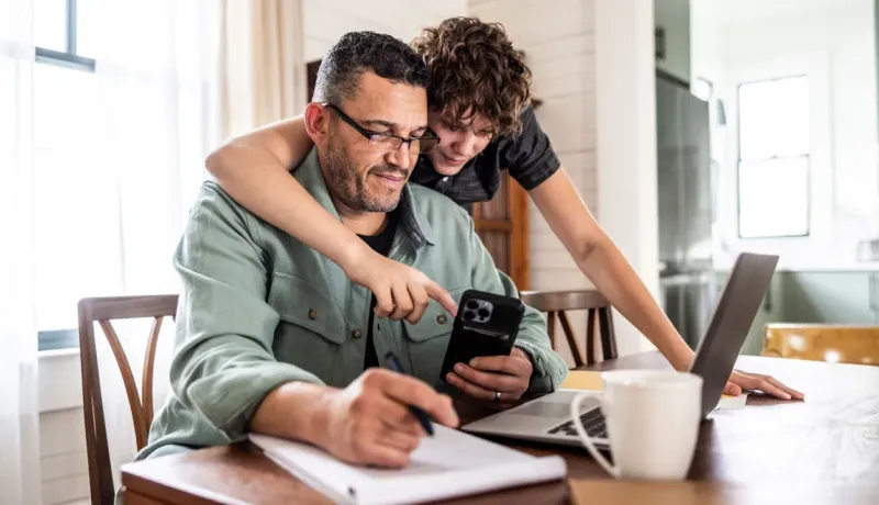 Un père travaille à la maison avec son fils consultant son téléphone.