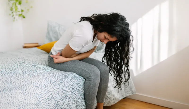 Une jeune femme se penche en avant sur son lit, se tenant le bas-ventre.