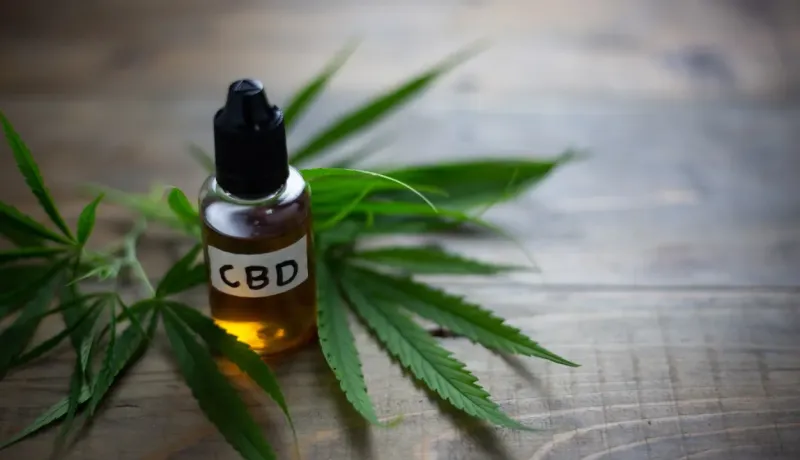 Flacon de CBD et feuilles de cannabis sur bois. Représentation du cannabidiol.