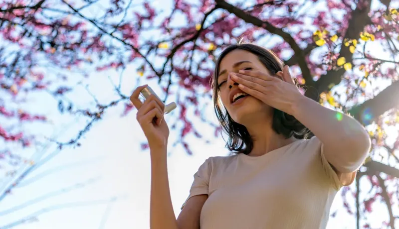 Une femme utilise un inhalateur sous un arbre en fleurs.