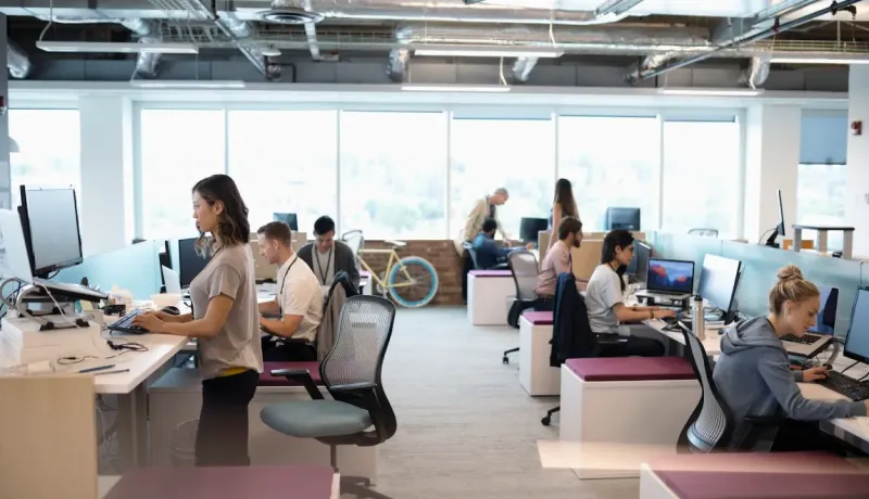 Espace de travail moderne et lumineux avec plusieurs employés travaillant sur ordinateurs.