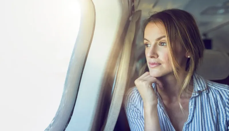 Une femme regarde par le hublot d'un avion, pensant à son voyage.