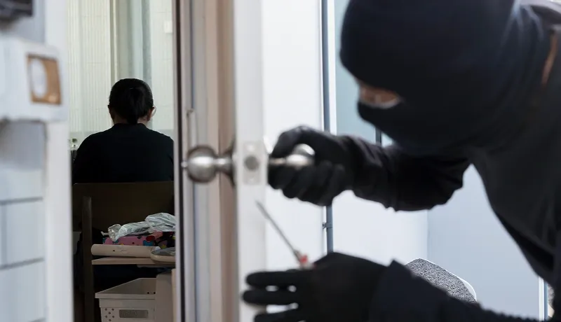 Un individu vêtu d'un hoodie noir observe une porte.