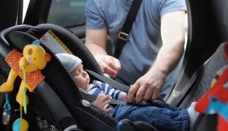 Un bébé attaché dans un siège auto, avec une personne ajustant les sangles.