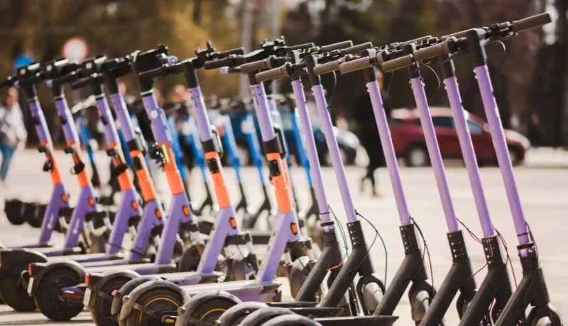 Une rangée de trottinettes violettes est alignée sur la rue.