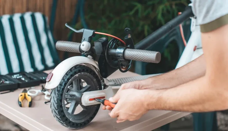 Un homme répare une roue de trottinette.