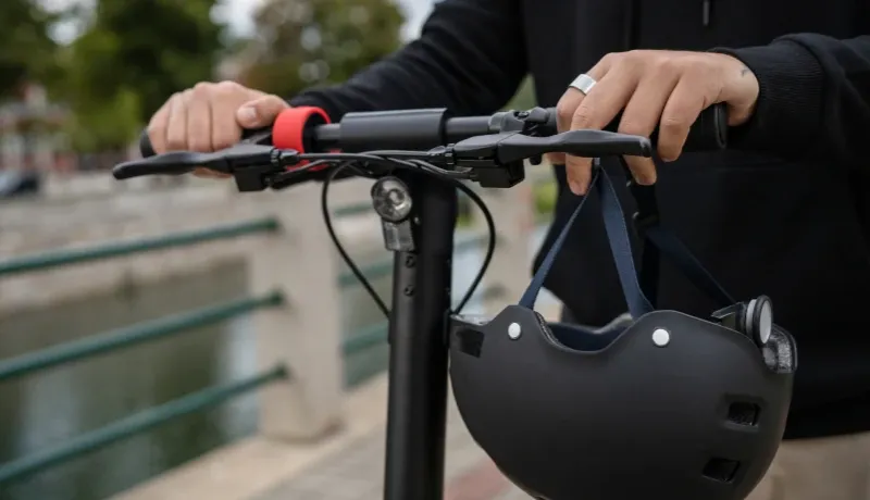 Une personne tient un casque sur une trottinette.