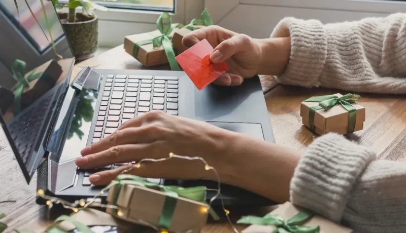 Achat de cadeaux en ligne. Gros plan sur des mains tapant sur un PC et tenant une carte de crédit entourées de paquets cadeaux.