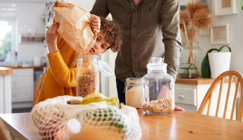 Enfant avec son père versant des céréales d'un sac en papier dans des bocaux en verre. Zéro déchet et cuisine.