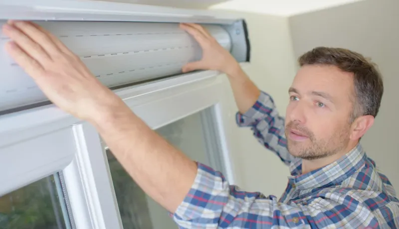 Gros plan sur un homme installant ou ajustant un volet roulant en aluminium sur une fenêtre intérieure. Bricolage.