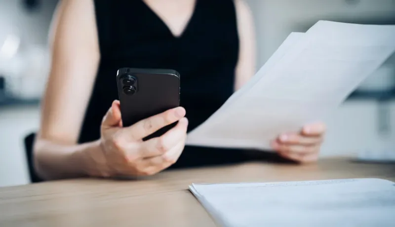 Gros plan sur une femme utilisant son smartphone pour scanner ou vérifier des informations sur des documents administratifs.