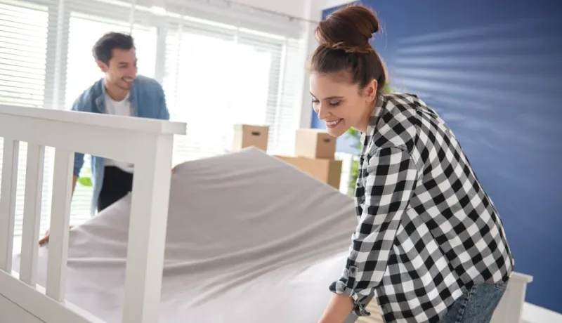 Un couple souriant défait son lit pour le déménagement. Ils retirent la housse de matelas. Ambiance de maison neuve.