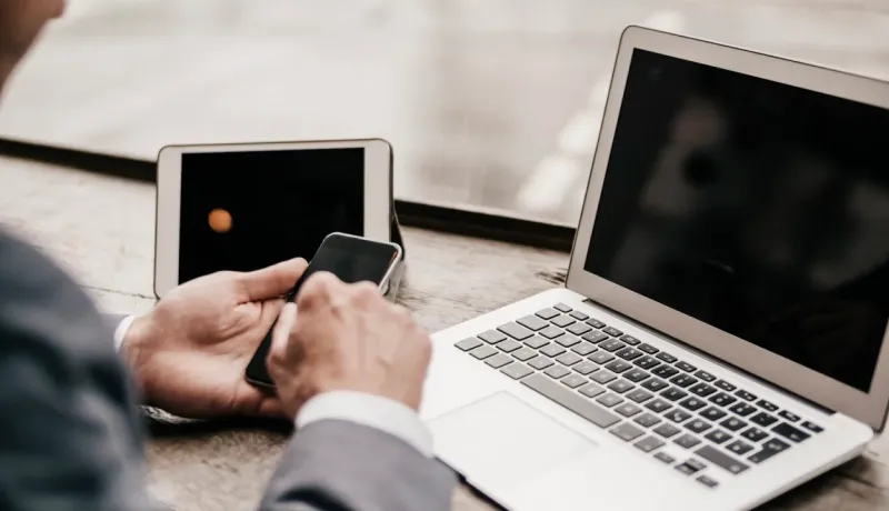 Gros plan sur les mains d'un homme en costume, utilisant un smartphone à côté d'une tablette et d'un ordinateur portable.