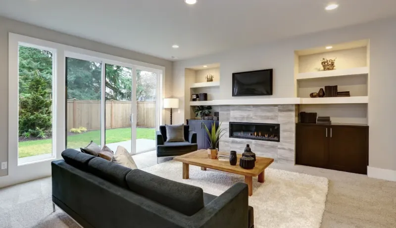 Salon moderne et épuré avec cheminée, télé et grandes baies vitrées donnant sur le jardin. Design intérieur.