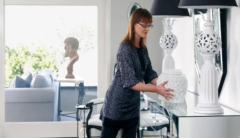 Une décoratrice ajuste un vase décoratif sur une console miroir. Décoration d'intérieur élégante.