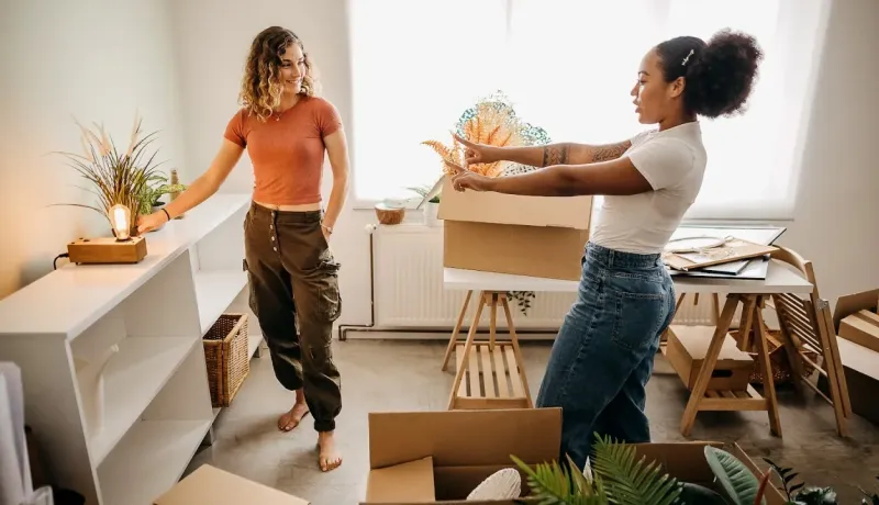 Deux femmes (colocataires/amies) s'amusent en déballant des cartons lors de leur emménagement dans un appartement lumineux.