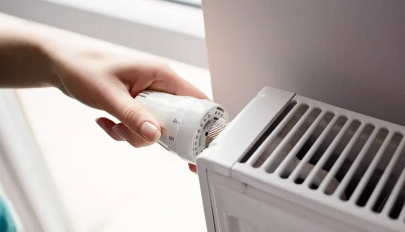 Gros plan sur une main ajustant le thermostat d'un radiateur blanc pour régler la température ambiante de la pièce.