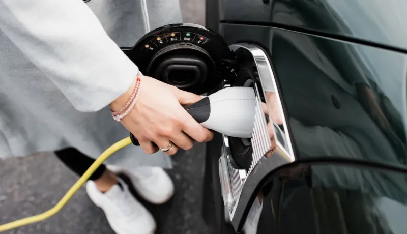 Gros plan sur une personne branchant un câble pour recharger une voiture électrique, le rabat du port de charge ouvert.