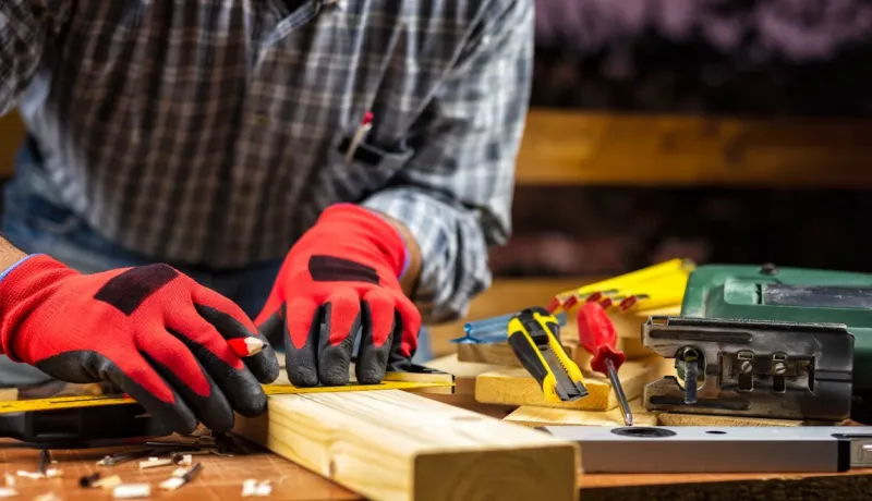 Gros plan sur les mains gantées d'un menuisier marquant une planche de bois avec un crayon et une équerre.