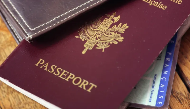 Gros plan sur un passeport français bordeaux et une carte d'identité, reposant sur un portefeuille en cuir marron.