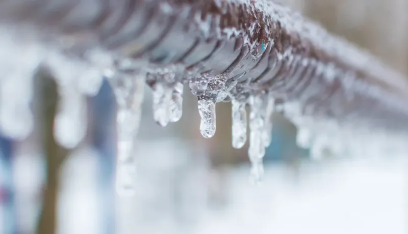 Gros plan sur une rampe ou une barre en métal recouverte de stalactites de glace transparentes par temps froid.