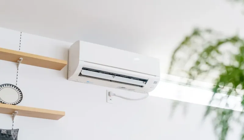 Unité de climatisation murale blanche installée dans une pièce moderne et lumineuse au-dessus d'étagères en bois.