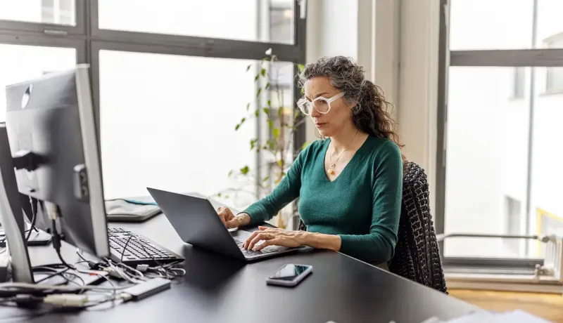 Une femme en chemise verte est assise à un bureau avec un ordinateur portable.